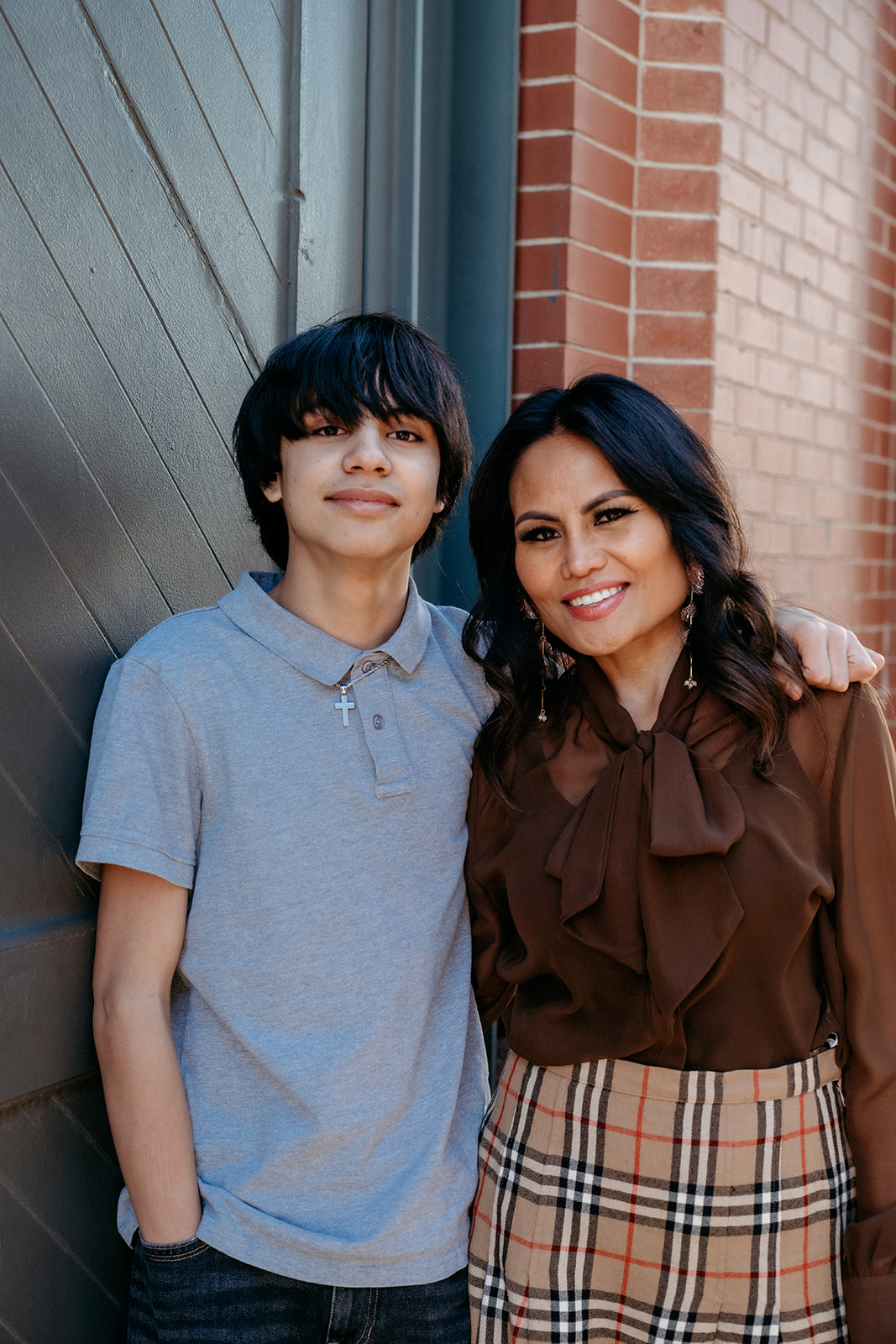 A mother standing arm in arm with her teenage son against a brick wall in Denver during a warm, relaxed family portrait session with Denver photographers.