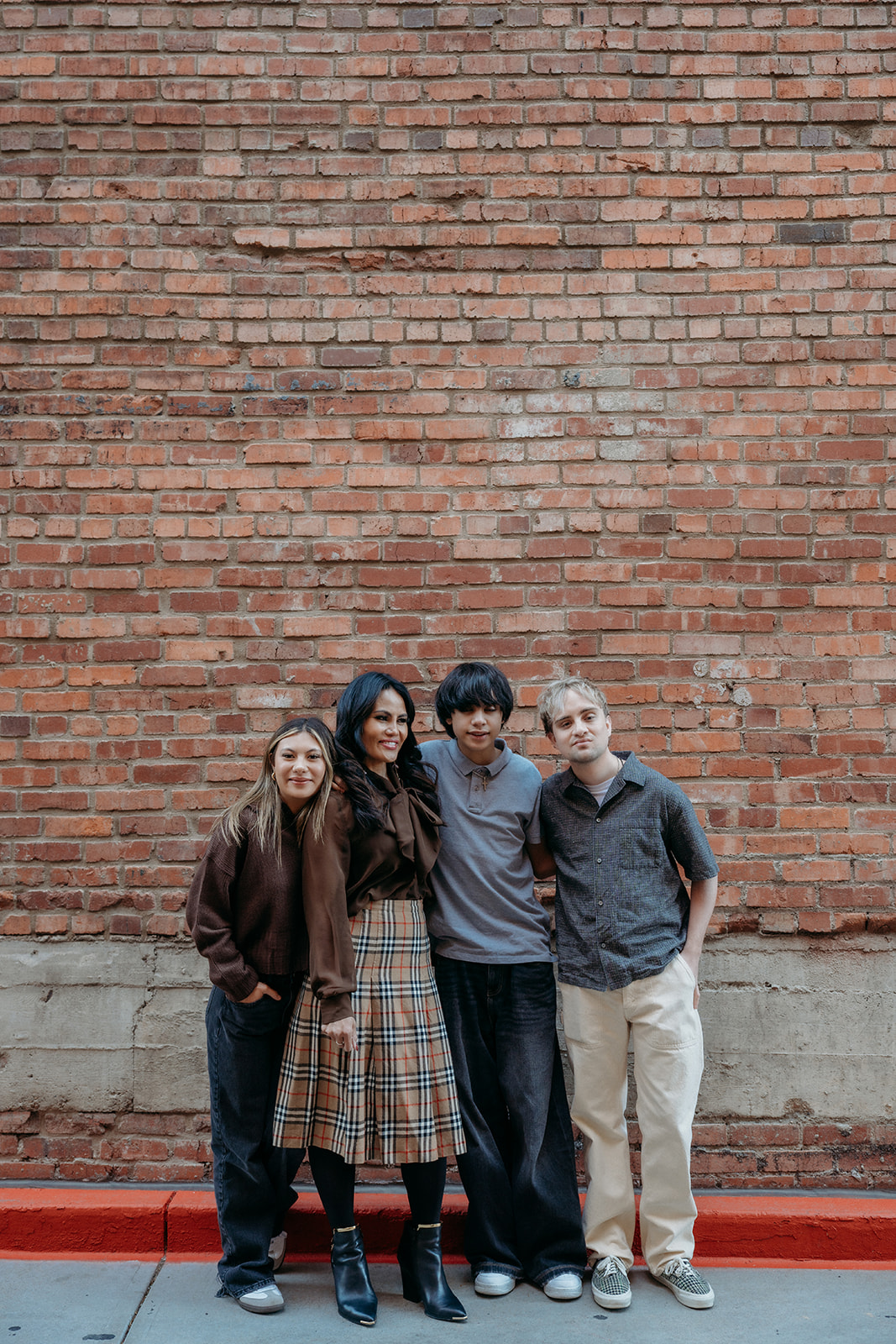Four siblings standing casually against a red brick wall in Denver, photographed in a relaxed, documentary style family session.