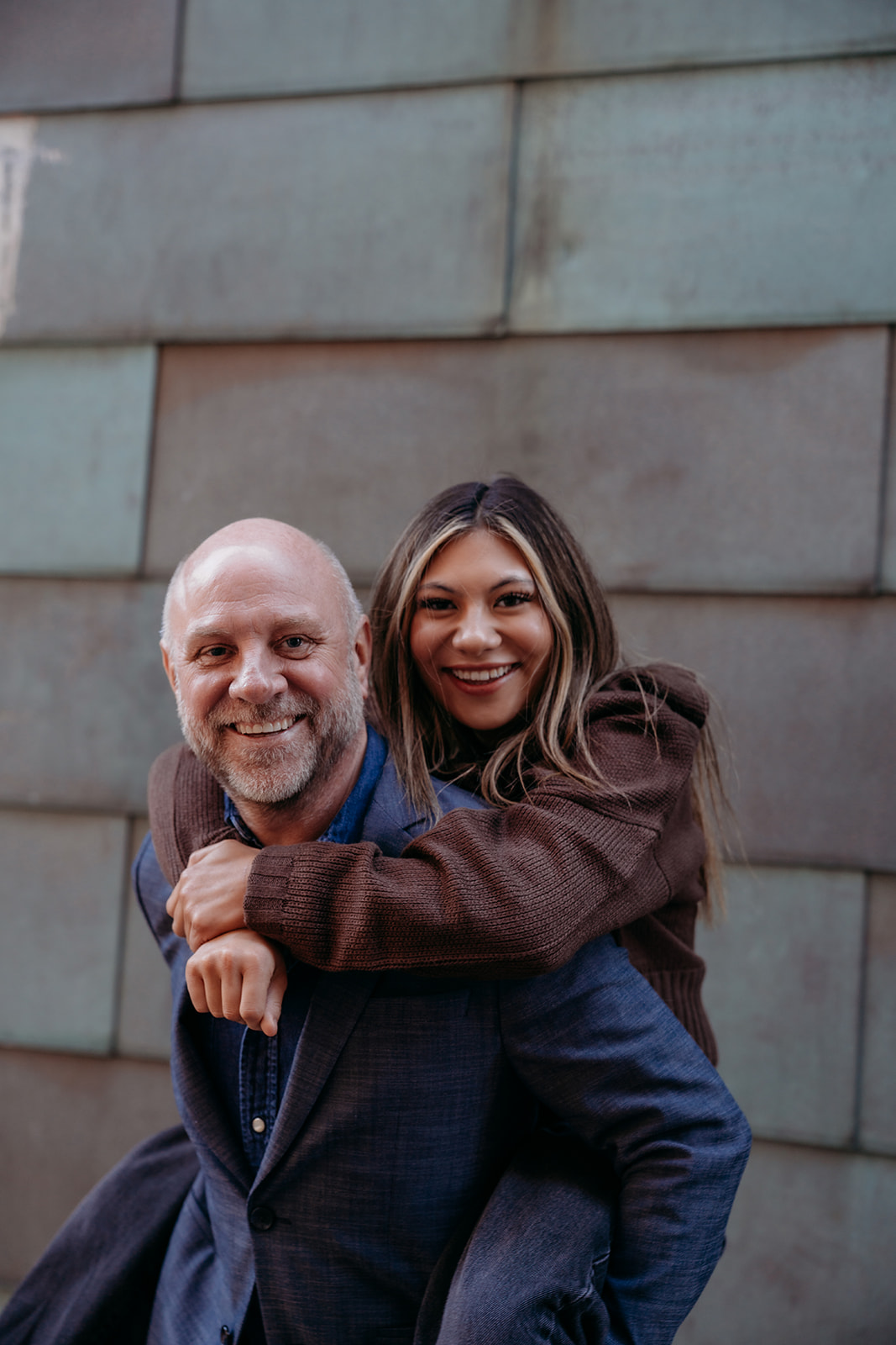 A woman hugging a man from behind, both smiling warmly during an intimate urban portrait session in Denver.