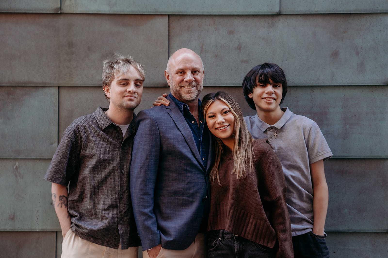 A father surrounded by his adult children, all smiling closely together during an urban family portrait session in Denver.