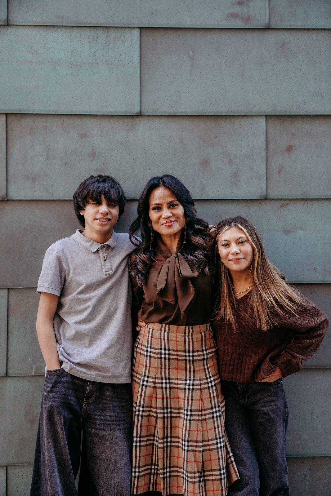 A mother standing between her two children against a textured wall in Denver, smiling during an urban family portrait session with Denver photographers.